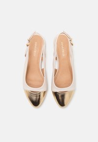 Scarpe slingback bianche con punta arrotondata, caratterizzate da una punta in oro metallico e una chiusura con fibbia laterale. Texture liscia e design minimal.