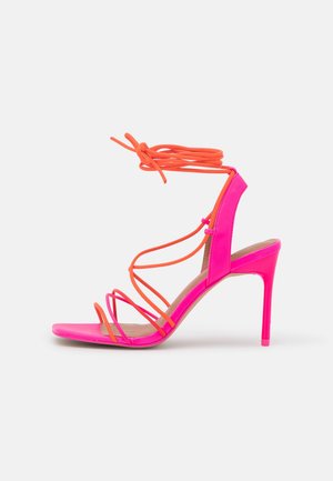 Pink high heel sandal with orange straps, featuring a sleek design and open toe. The heel has a glossy finish and minimalistic detailing.