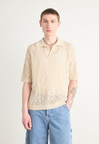 Strikket polo skjorte i off-white med løs passform, kort ermer og åpen gitterdesign; har en myk tekstur og krage.