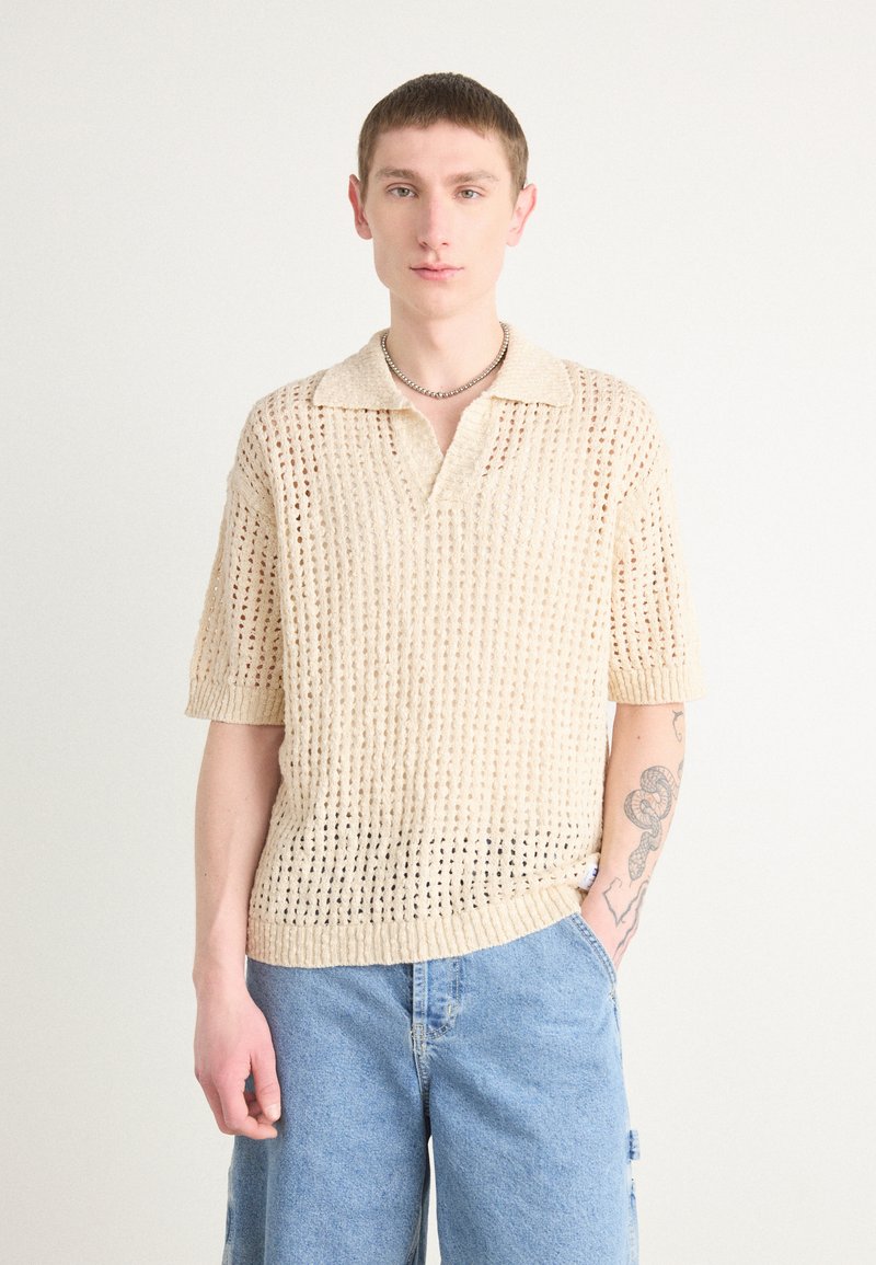 Strikket polo skjorte i off-white med løs passform, kort ermer og åpen gitterdesign; har en myk tekstur og krage.