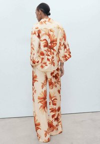 Floral print shirt and pants set, featuring an orange and beige color scheme, loose fit, and textured fabric with a palm leaf pattern.