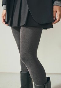 Gray stretchy leggings paired with a black pleated skirt and a black blazer. The leggings have a smooth texture and fitted shape.