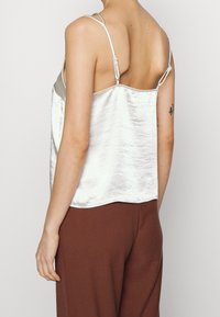 Silver satin camisole with adjustable straps, smooth texture, and a straight hem, paired with brown high-waisted pants.