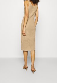 Gebreid midi-jurk in beige, met een textuurpatroon en een ronde hals. Slanke pasvorm met een rechte zoom, gedragen met lichte hoge hakken.