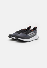 Chaussures de sport avec une tige en mesh noir, des rayures grises et des accents rouges. Dotées d'un semelle intermédiaire blanche légère et d'une semelle extérieure noire texturée.