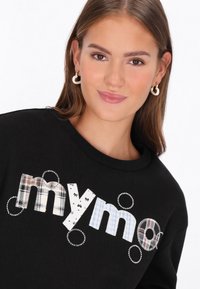 Fekete pulóver, amelyen a "mymo" szó színes mintákkal és kör alakú díszítésekkel szerepel. Kerek nyakkivágás és puha anyag.