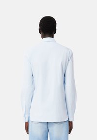 Camisa de manga larga azul clara con cuello abotonado, que presenta un sutil patrón de rayas y puños ajustables, hecha de un tejido suave.