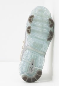 Semelle d'une basket blanche avec des unités de coussin d'air transparentes et des patins de traction en caoutchouc marron sur fond blanc.