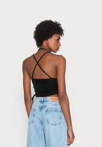 Top cropped preto com alças finas e detalhe torcido nas costas, combinado com jeans de cintura alta azul claros.