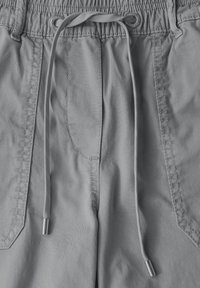 Shorts gris clair avec une taille à cordon de serrage, accents en métal sur les aglets et des coutures le long des poches latérales. Texture de tissu lisse.