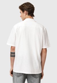 Hvid kortærmet skjorte i letvægtigt stof med en tekstureret overflade. Har en klassisk krave og detaljer i ryggen. Grå jeans er synlige.