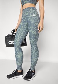 Leggings con un motivo astratto verde e blu, design a vita alta, abbinate a sneakers nere e a una borsa a tracolla nera con un logo.