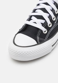 Svart kanvas sneaker med vita snörningar, vit gummitå, och en texturerad vit sula med diamantmönster. Accentuerad med svarta sömmar.