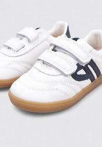 Zapatillas blancas con acentos en azul marino, dos tiras de velcro, suela de goma, parte superior texturizada y detalles de costura para un diseño añadido.