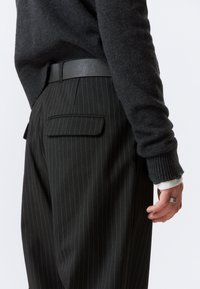 Czarne spodnie w paski z dwoma tylnymi kieszeniami, w połączeniu z ciemnym swetrem. Posiadają gładki czarny pasek i ściągacze na rękawach.