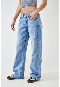 Vaqueros de pierna ancha en un azul claro, confeccionados en denim, con una cintura alta, bolsillos frontales y una textura desgastada. Combinados con zapatillas oscuras.