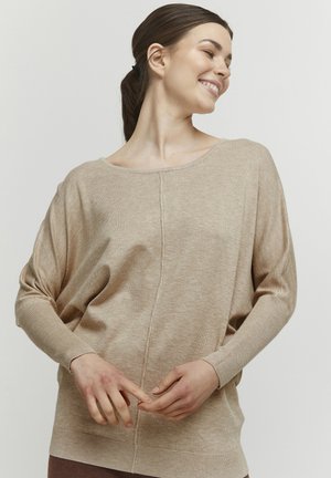 Beige pletený svetr s volným, širokým výstřihem a spadlými rameny. Obsahuje středový šev a vroubkované manžety pro texturu a detail.