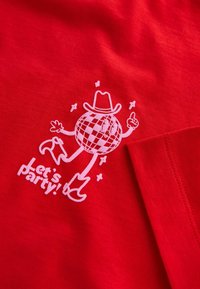 Red cotton t-shirt featuring white graphic of a disco ball character with a cowboy hat, cowboy boots, and the text “Let’s party!”