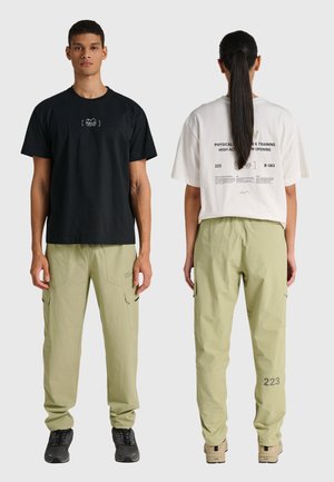 Twee modellen dragen lichtgroene cargobroeken; één in een zwart T-shirt met het gezicht naar voren, de ander in een wit bedrukt T-shirt met het gezicht naar achteren.