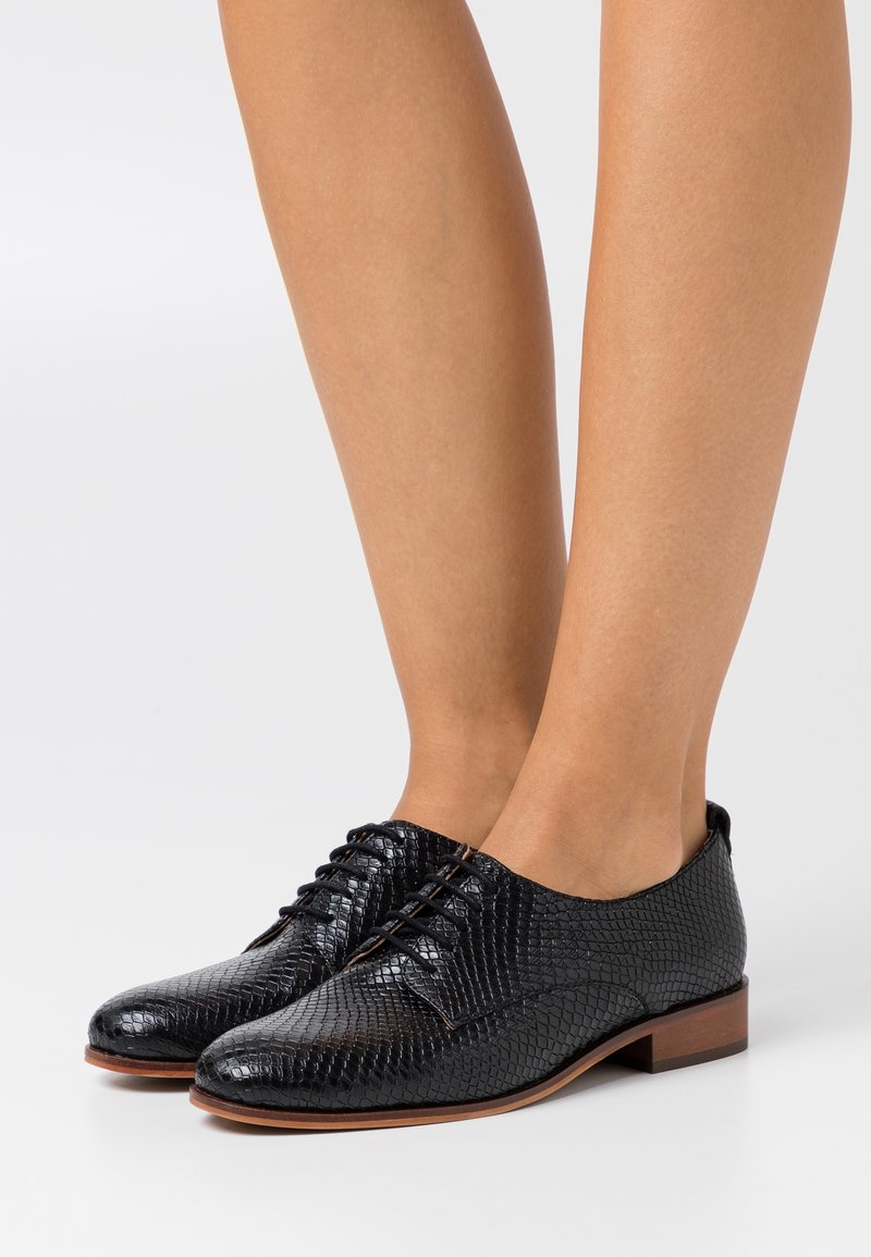 Chaussures oxford noires à lacets en matériau texturé avec un motif en imprimé serpent et un faible talon en bois. Fini lisse.