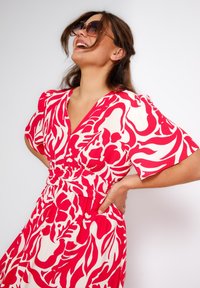 Rood en wit bloemenpatroon jurk met korte mouwen, een V-hals en een nauwsluitende taille, gemaakt van lichtgewicht stof met een gladde textuur.