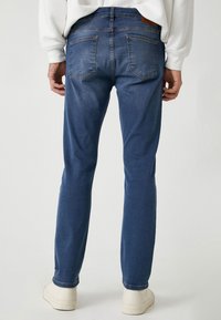 Jeans da uomo in denim blu con vestibilità dritta, design a cinque tasche e tessuto testurizzato. Presentano cuciture visibili e una patch in pelle con il marchio.