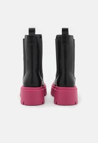 Musta nahkasaappaat nilkkapituisena, jossa on sileä pinta, ja joita koristaa paksu vaaleanpunainen pohja ja takana oleva vetotasku. Sivujen elastiset panelit helpottavat pukemista.