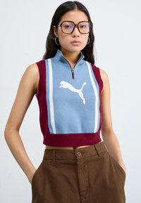 Puma ermeløs kort genser i lys blå og maroon, med halv glidelås, hvit logo og sidelister. Bomullsblanding med en glatt tekstur.