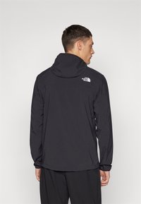 Schwarze wasserdichte Jacke mit Kapuze, mit einem Logo auf dem Rücken und langen Ärmeln. Glatte Textur, minimalistisches Design, geeignet für den Outdoor-Einsatz.
