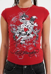 Rood T-shirt met korte mouwen met een schedelafbeelding met een hart, omringd door de tekst "DEATH OR GLORY" en verschillende decoratieve elementen.
