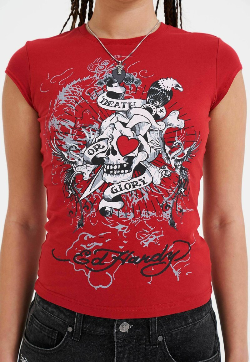 Rood T-shirt met korte mouwen met een schedelafbeelding met een hart, omringd door de tekst "DEATH OR GLORY" en verschillende decoratieve elementen.