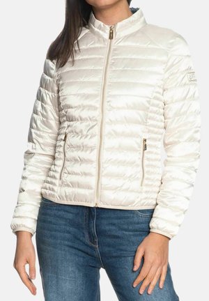 Donna che indossa una giacca trapuntata bianca con zip e tasche con zip, abbinata a jeans blu, mostrata dal collo ai fianchi.