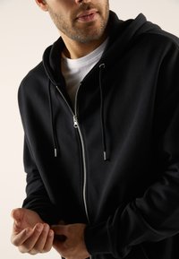 Black zip-up hoodie made of soft fabric, featuring a durable zipper, drawstring hood, and kangaroo pockets for added convenience.