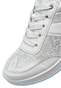 White sneaker with textured snake-skin pattern on upper, thick white laces, and light blue rubber sole visible at the toe.