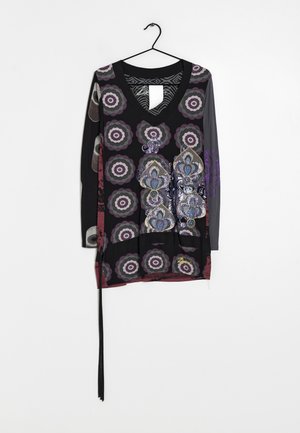 Zwarte top met lange mouwen en V-hals met paarse, grijze cirkelpatronen en blauwe bloemmotieven, hangend aan een zwarte hanger tegen een witte achtergrond.