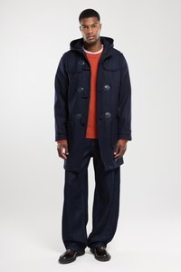 Cappotto duffle in lana blu navy con cappuccio, chiusure a scorrimento e tasche ampie. Abbinato a un maglione in lana arancione e pantaloni in denim scuri a gamba larga.