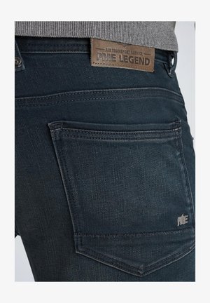 Donkerblauwe denim jeans met een gestructureerde afwerking, voorzien van een leren patch met het label "PME Legend" en een achterzak met subtiele borduursels.