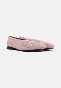 Un par de bailarinas rosas con bordado floral y tacones bajos negros sobre un fondo blanco sencillo.