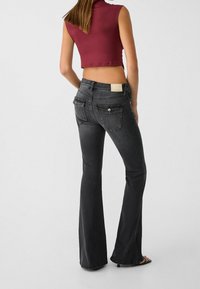 Pantalones vaqueros de campana negros con una textura suave, que cuentan con dos bolsillos traseros y una etiqueta de color beige claro en la cintura.