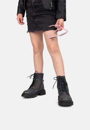 Bottines noires à talons hauts et lacets avec une finition irisée brillante, semelles en caoutchouc épaisses et détail de fermeture éclair sur le côté. Portées avec une jupe en denim noire.