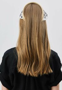 Schwarzes Stoffhemd, das von einer Person mit langen, glatten, blonden Haaren getragen wird. Ein gemustertes Accessoire befindet sich hinten am Kopf.