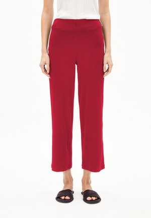 Pantalons rouge à jambe large avec une taille élastique haute, fabriqués à partir d'un tissu doux et lisse ; portés avec des sandales à glissière noires.