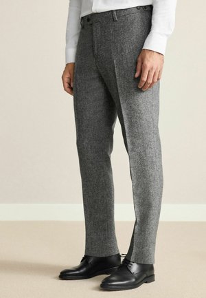 Graue Wollhosen mit strukturiertem Finish, schmalem Schnitt und seitlichen Taschen, kombiniert mit schwarzen Lederschuhen. Maßgeschneiderter Schnitt und flacher Bund.