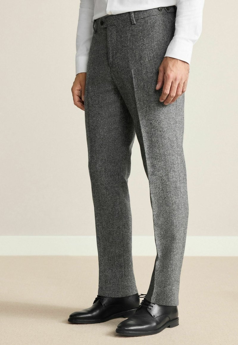 Gray wool trousers with a textured finish, slim fit, and side pockets, paired with black leather shoes. Tailored design and flat front.