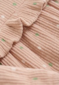 Rosa Rippstoff mit grünen und weißen Punkten, versehen mit einer fransigen Kante. Die Oberfläche wirkt weich und plüschig.