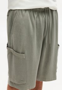 Lys grønne cargo shorts lavet af struktureret stof, med sidelommer og en elastisk talje med snor til justering.