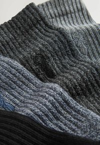 Patru perechi de șosete tricotate în gri închis, gri deschis și negru, având o textură ribbed și broderie logo subtilă.