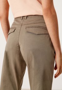 Pantaloni khaki con una texture liscia, dotati di due tasche posteriori e una vita aderente. Il materiale appare leggero e casual.