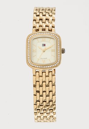 Reloj de pulsera enlazado en tono dorado con esfera cuadrada, bisel adornado con cristales, números romanos y un pequeño logo de Tommy Hilfiger debajo de la marca de las 12.