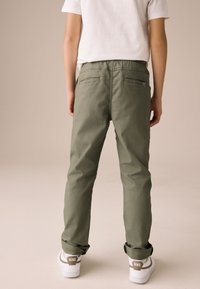 Beżowe spodnie o luźnym kroju, z elastycznym paskiem w talii, dwoma kieszeniami z tyłu i podwiniętymi nogawkami, zestawione z białymi trampkami z brązowym akcentem.